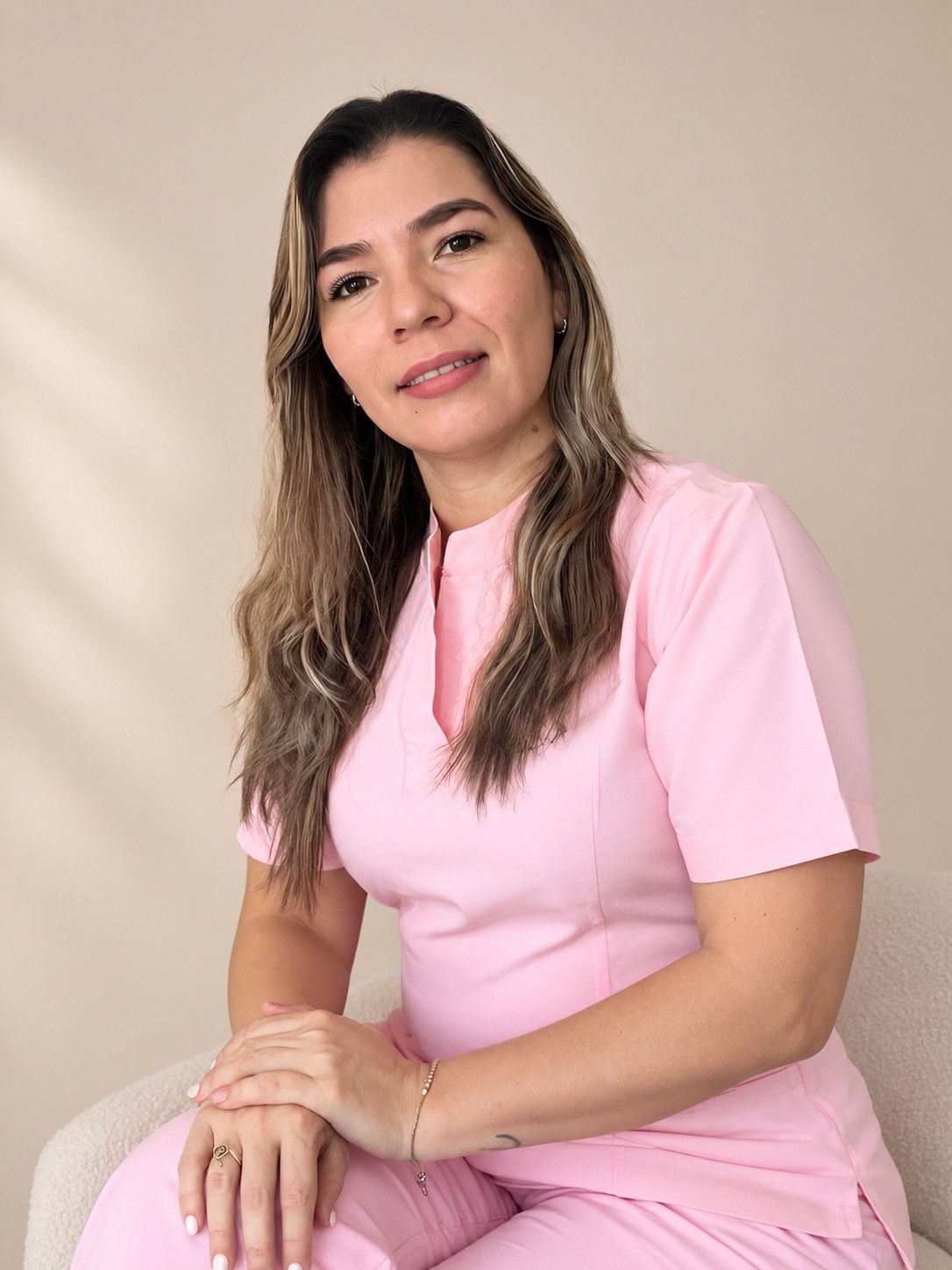 Jennyfer Gonzalez sentada con uniforme rosa sobre un fondo beige luminoso